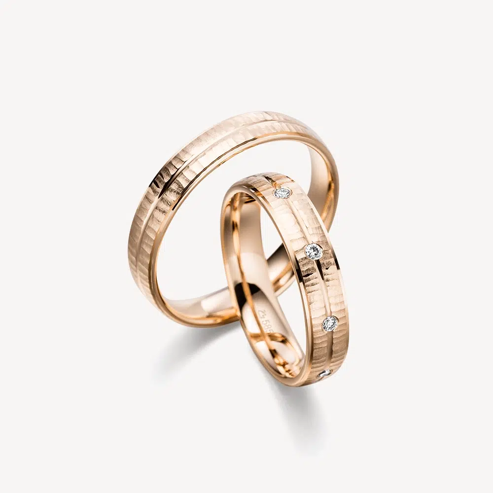 Love Train Trauringe von DAVINÉL im Paar: Herrenring in Roségold mit quer verlaufender Reliefstruktur, Damenring in Roségold mit neun Brillanten im Brillantschliff